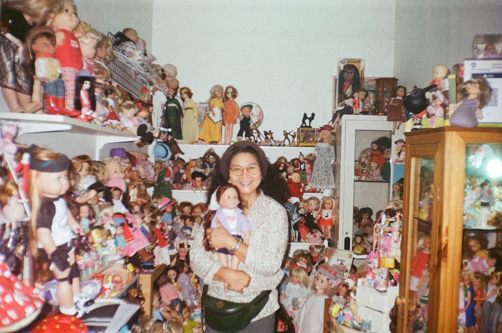 Женщина держит в руках куклу, вокруг ещё множество кукол