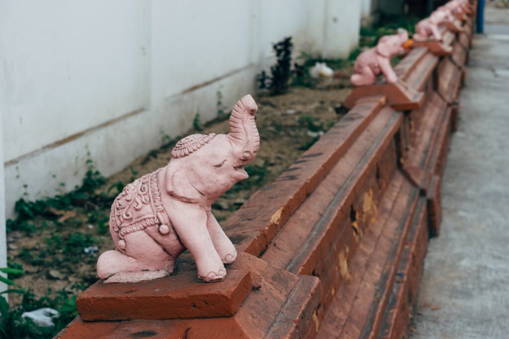 Розовая статуэтка слона на заборе