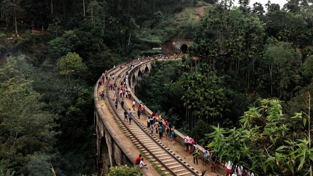 Люди, идущие вдоль железнодорожных рельс на мосту посреди джунглей