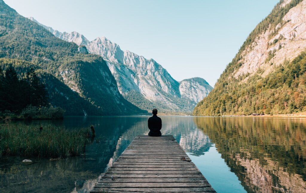 Одинокий человек на мостках смотрит на тихое горное озеро