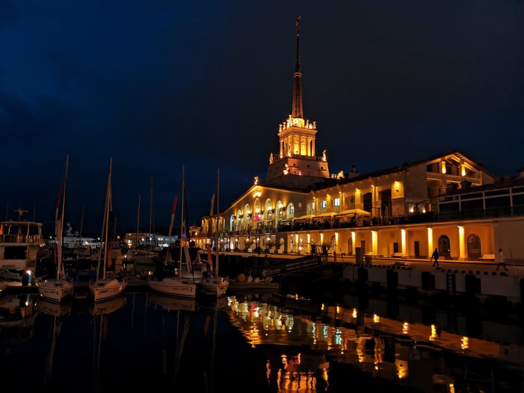 Освещенное ночное здание со шпилем и яхты на причале