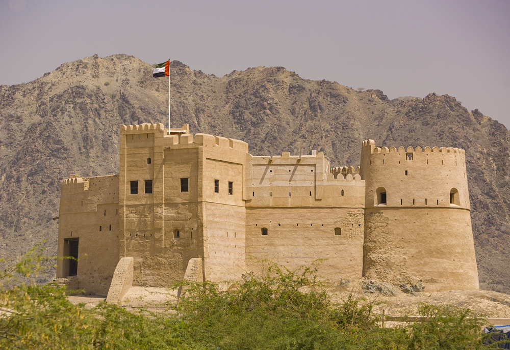 Крепость на фоне гор с флагом ОАЭ